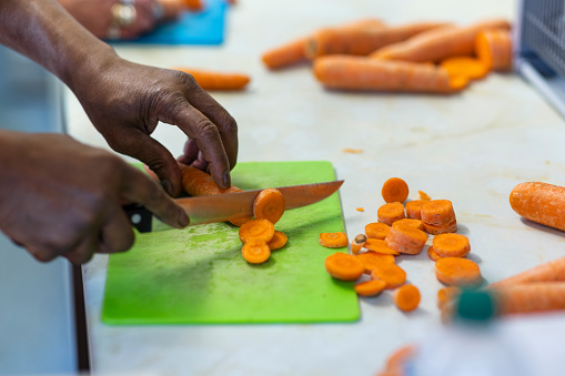 Side view close up of a volunteer working in a soup kitchen/food bank, chopping carrots and preparing food in the North East of England.