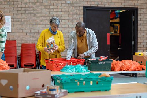 Group of volunteers organising food donations onto tables at a food bank in the North East of England. They are working together, setting up sections of the room in a church.