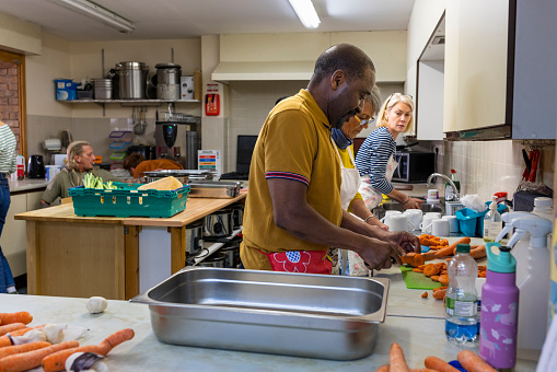 Side view of volunteers working in a soup kitchen/food bank together, preparing food, chopping vegetables. They are in the North East of England.