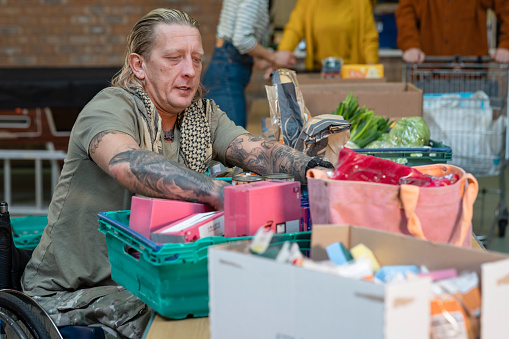 Group of volunteers organising food donations onto tables at a food bank in the North East of England. Focus is on one man who is in a wheelchair using a organising his section.