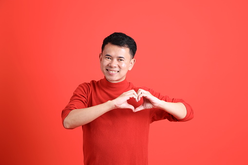 The Asian LGBTQ man with red shirt standing on the orange background.