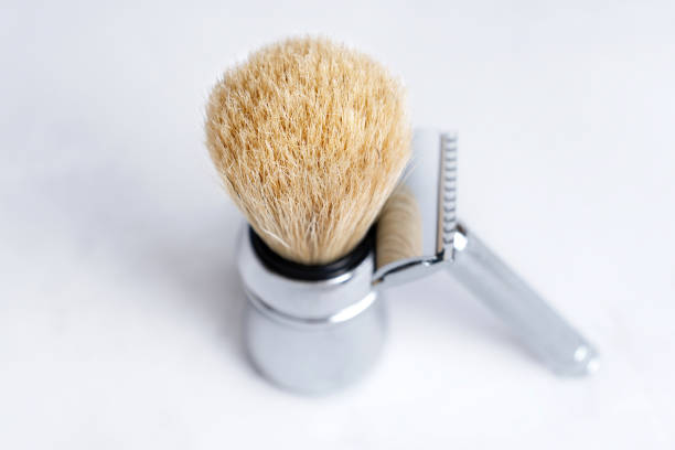 Chrome-plated safety razor and shaving brush isolated on light gray background.