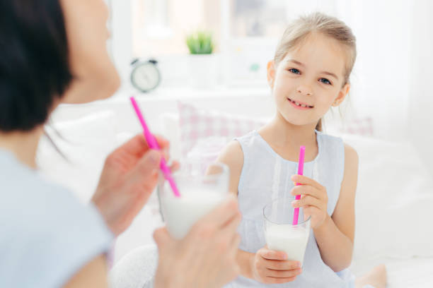 istock Pretty cute small child drinks delicious cocktail, has pleasant talk with her affectionate mother, enjoy together good morning, plan what to do during day off. Light tones. Spacious cozy bedroom 1408439023