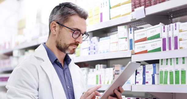 istock Pharmacist in a pharmacy using a digital tablet to sort an inventory of retail medication on a shelf. Mature man using technology to stay organised while counting and checking stock in a drugstore 1408439077