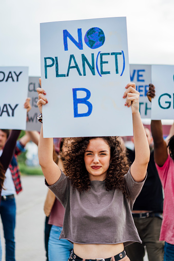 Group of protestors holding hand-made signs on cardboards and marching together in the city streets against climate change