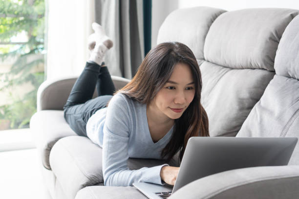 istock Happy woman lying down on sofa using laptop communicating online at home. Smiling girl working on computer, enjoying internet shopping or chatting in social networks. Technology and lifestyle concept. 1408448694