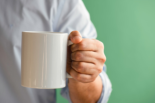 Man holding white coffee cup, green background.
