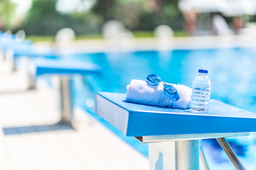 Swimming goggles, towel and water bottle placed on the starting bridge by the swimming pool.