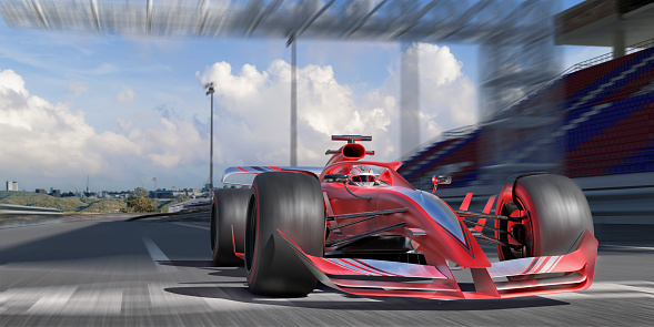 A contemporary generic red and silver race car driven at high speed on a racetrack past an empty grandstand, over the finish line. There is motion blur on the wheels and background. It's a bright sunny day with some clouds in the sky. Location is fictional.