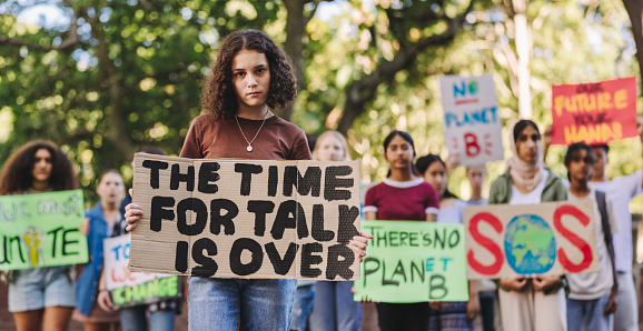 Teenage girl looking at the camera while leading a march against climate change. Group of multiethnic youth activists protesting against global warming. Young people joining the global climate strike.