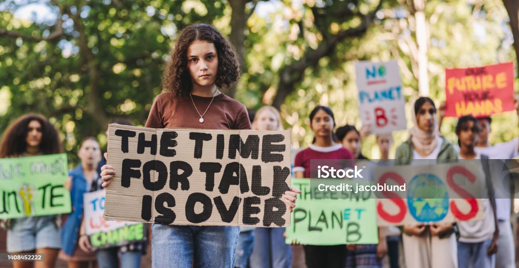Teenage girl leading a march against climate change Teenage girl looking at the camera while leading a march against climate change. Group of multiethnic youth activists protesting against global warming. Young people joining the global climate strike. Child Stock Photo