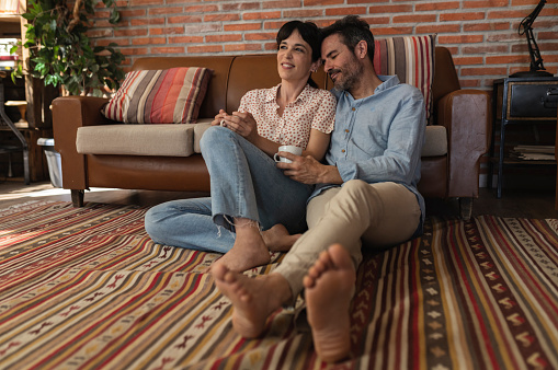 A middle-aged married couple is relaxing in the living room at home barefoot on the floor