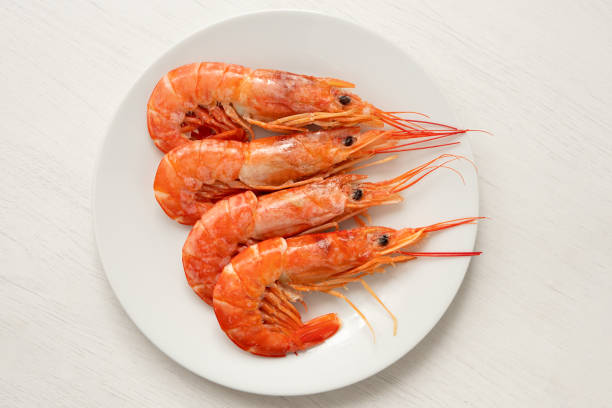 Four cooked red tiger shrimps on a white ceramic plate isolated on white painted wood. Top view.