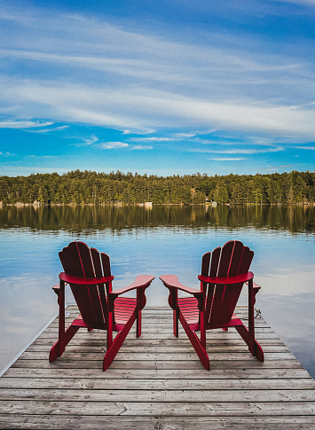 Dos sillas rojas adirondack en el extremo de un muelle con vistas a un lago. photo