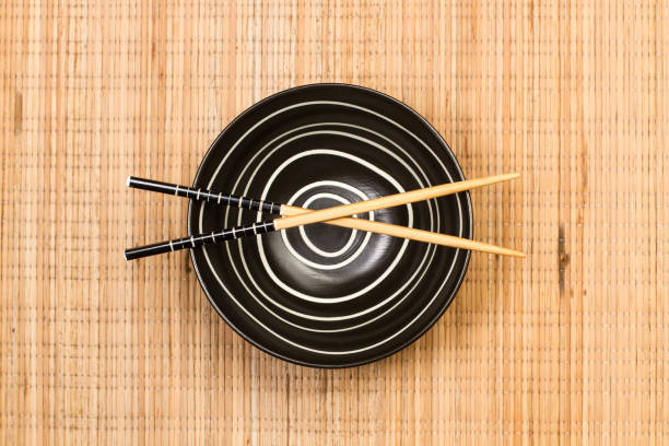 Black bowl and chopsticks on a bamboo table mat in a top view