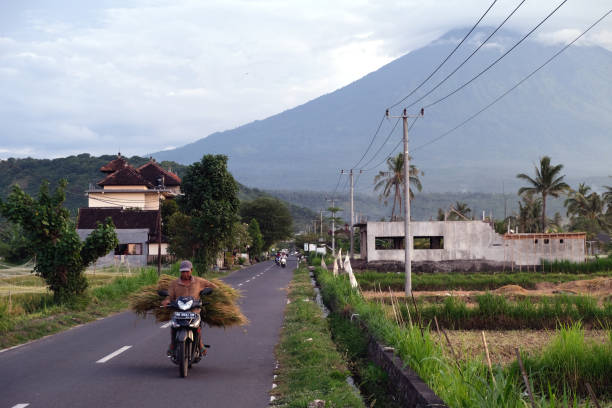 Local man riding motorcycle in Amed, a village on the east coast of Bali. In the distance the mount Agung, an active volcano and the highest point on Bali at 3031 mt.