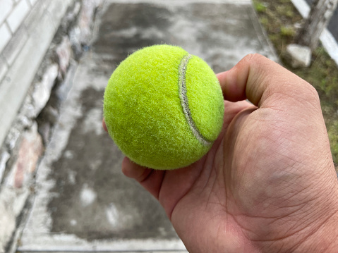 A hand holds a green tennis ball in the middle of the fairway