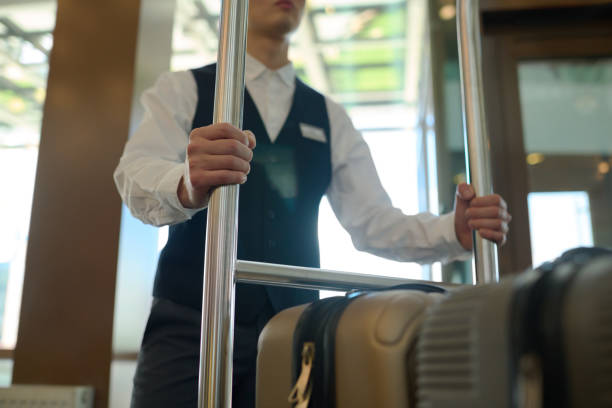 制服を着た若いベルのクロップドショットがカートの金属製のハンドルで握られている - luggage cart ストックフォトと画像