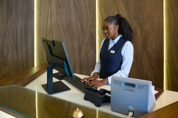 young serious female receptionist entering personal data of hotel guests - airport check in counter imagens e fotografias de stock