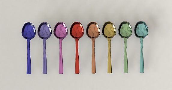 Pastel colored metal spoons arranged on a plain background.