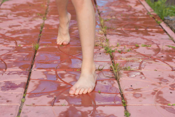 Child legs and feet walking in puddle water with mud barefoot during summer day