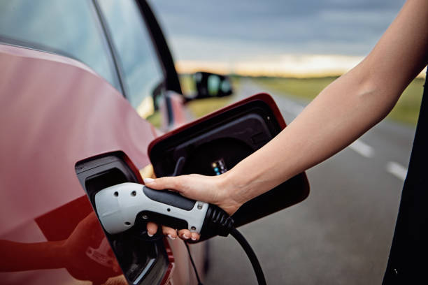 woman is plugging/unplugging cable to electric car - fuel efficiency imagens e fotografias de stock