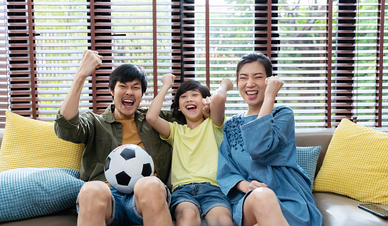 Asian family watching football sports games on TV and reacting happy exiting when team Shoot the ball into the goal.