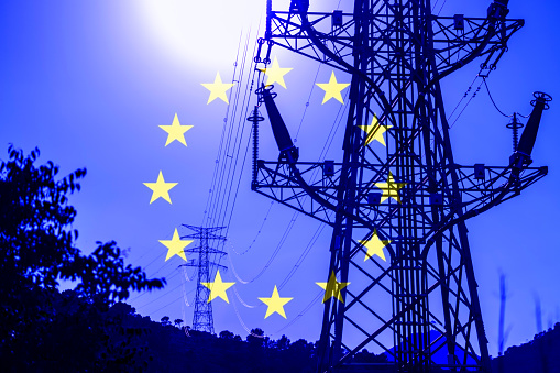 Composite image with high voltage electrical towers and the European flag in the background. European energy crisis concept.