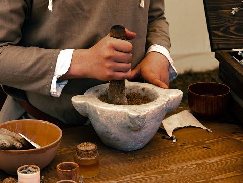 medieval reenactment - herbalist table person grinds seeds with mortar and pestle to create a dough