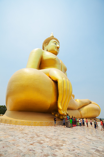 Golden thai buddha statue and landmark  at Wat Muang and group of praying thai people in front of statue in Ang Thong with national landmark 96m high Buddha statue of Thailand  in public free ground outside of city. People are touching fingers of statue