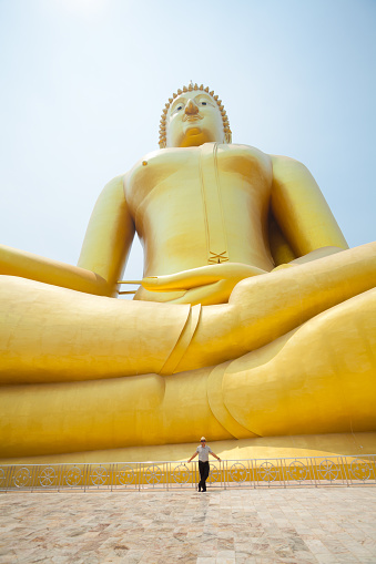 A man is standing in front of giant golden thai buddha statue and landmark   at Wat Muang  in Ang Thong with national landmark 96m high Buddha statue of Thailand  in public free ground outside of city
