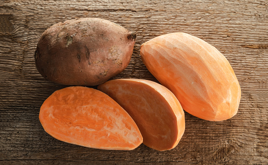 Peeled and unpeeled sweet potato roots on a rough wooden table. Selective focus.