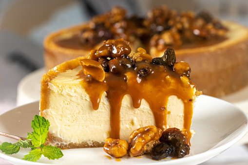 Portion of Caramel cheesecake with nuts on white table with cutlery and nuts