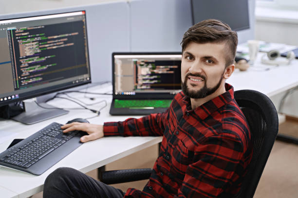 Computer programmer developer working in IT office, sitting at desk and coding, working on a project in software development company or startup stock photo