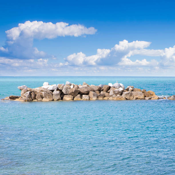 una baia tranquilla con paesaggio marino, acqua, cielo nuvoloso e frangiflutti di roccia - immagine con spazio di copia - marina di pisa foto e immagini stock