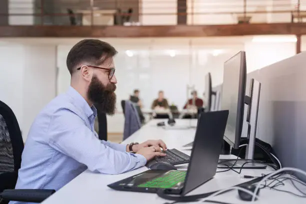 Photo of Senior computer programmer developer working in IT office, sitting at desk and coding, working on a project in software development company or startup