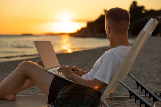 istock Man admiring the sunset on the beach, while working on laptop 1408496457