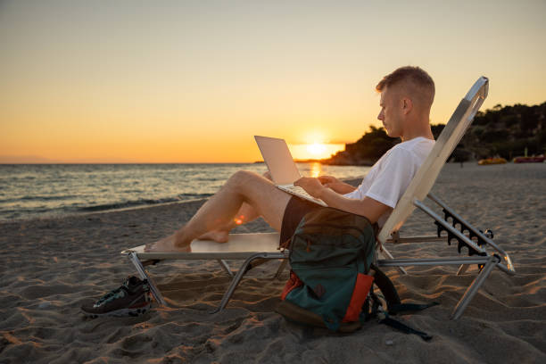 istock During sunset on the beach, Caucasian young man working on laptop 1408497130