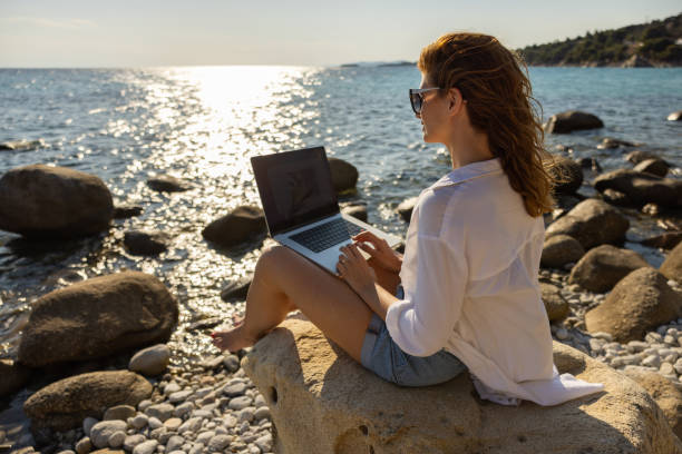 istock Female freelancer working on laptop, from the rocky beach 1408497583