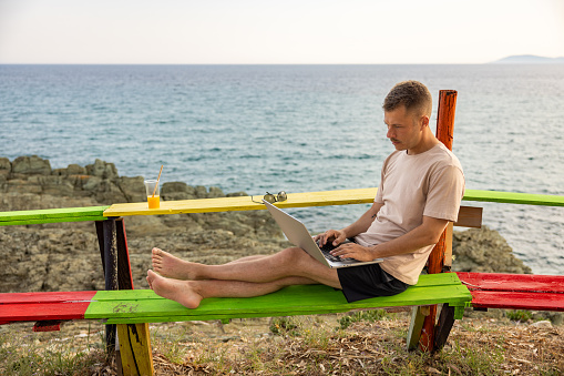 Caucasian young man working on laptop, from the beach bar during his summer vacation