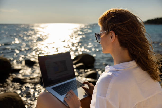 istock Female freelancer working on laptop, from the rocky beach 1408497685