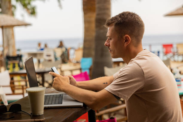 istock Man using mobile phone, while working on laptop  from the beach coffee shop 1408499088