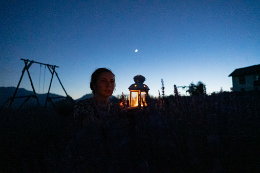 Farmer woman holding lantern in the lavender field during night, front of farm house