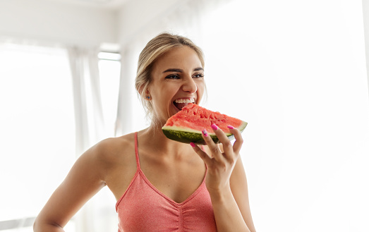 Young woman enjoying slice of watermelon after home fitness routine