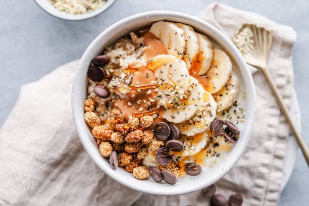 Bowl of oatmeal with banana, dried mulberries, peanut butter and chocolate chips Overhead view of a bowl of oatmeal topped with banana slices, dried mulberries, peanut butter, chocolate chips, hemp seeds and chia seeds porridge stock pictures, royalty-free photos & images