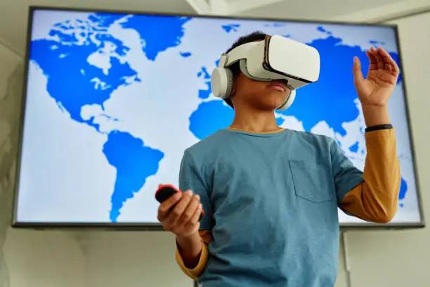Waist up portrait of young black boy using VR technology in school classroom with geography map in background, copy space