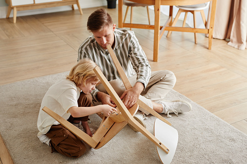 High angle portrait of father and son assembling wooden furniture together at home in earthy cozy tones