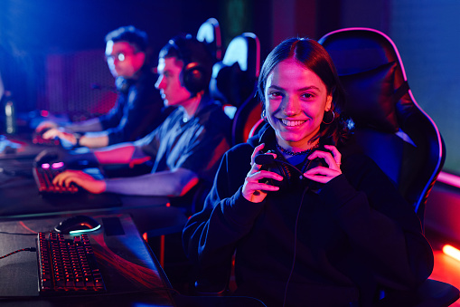 Portrait of young woman on cyber sports team smiling at camera cheerfully lit by neon light, copy space