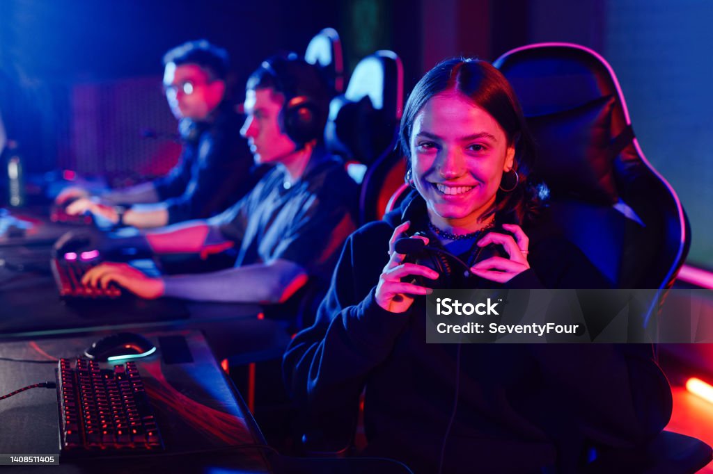 Girl in Video Game Club Portrait of young woman on cyber sports team smiling at camera cheerfully lit by neon light, copy space Neon Lighting Stock Photo