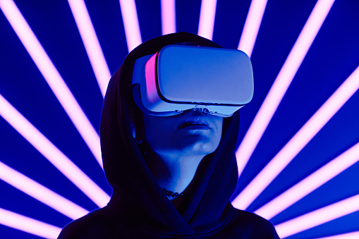 Futuristic shot of young woman wearing VR headset with neon light beams in background, copy space